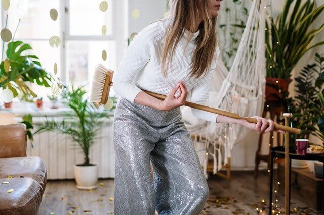 Woman playfully holding a broom in a decorated living room demonstrating cleaning habits