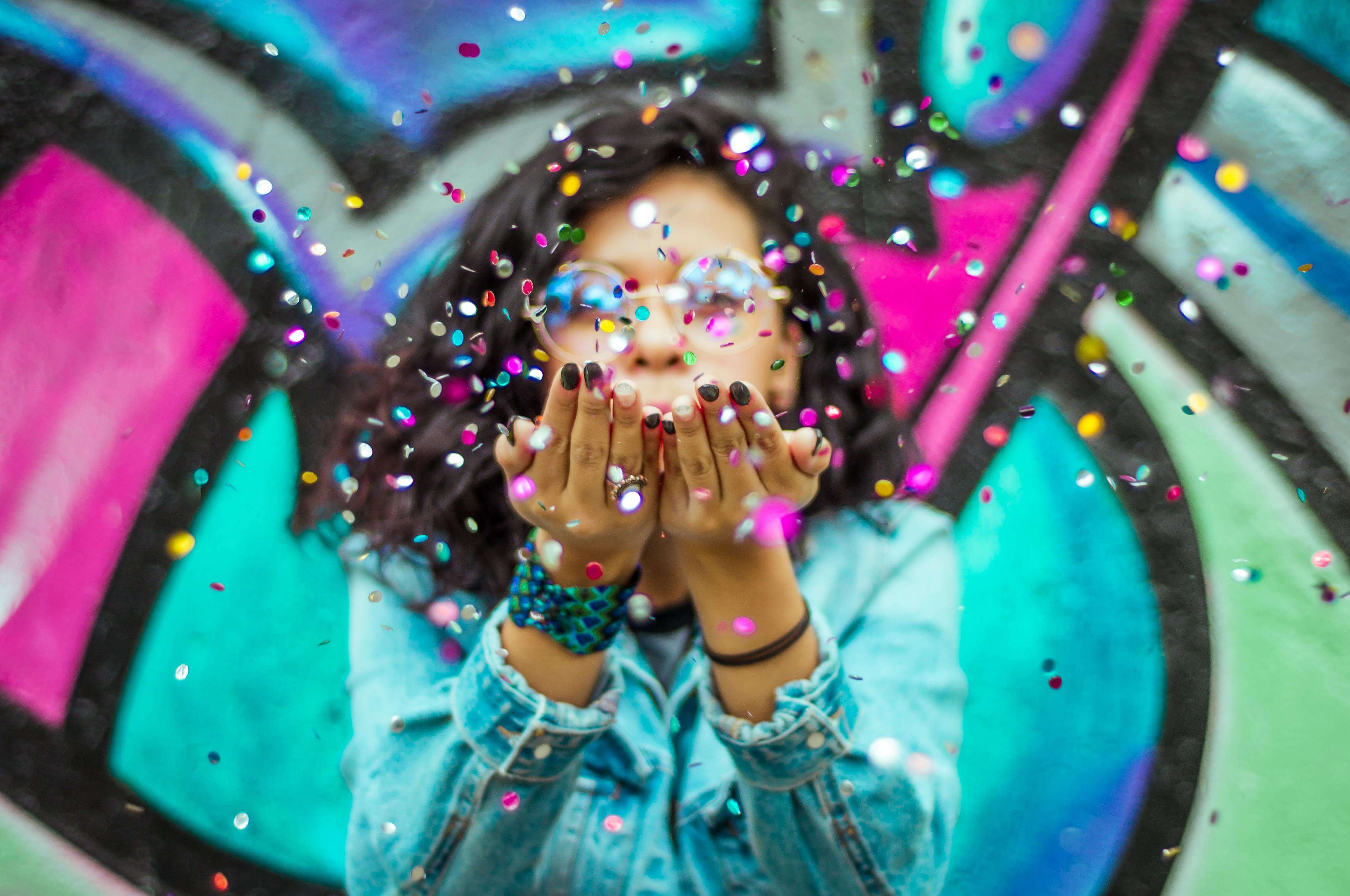 Woman blowing colorful confetti with vibrant graffiti background HAPPY SiNKS in 60 seconds