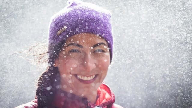 Smiling woman wearing purple beanie in snowy outdoor winter setting promoting essential oils to boost wellbeing